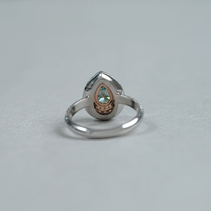 back view of green pear cut diamond double halo engagement ring on grey fabric