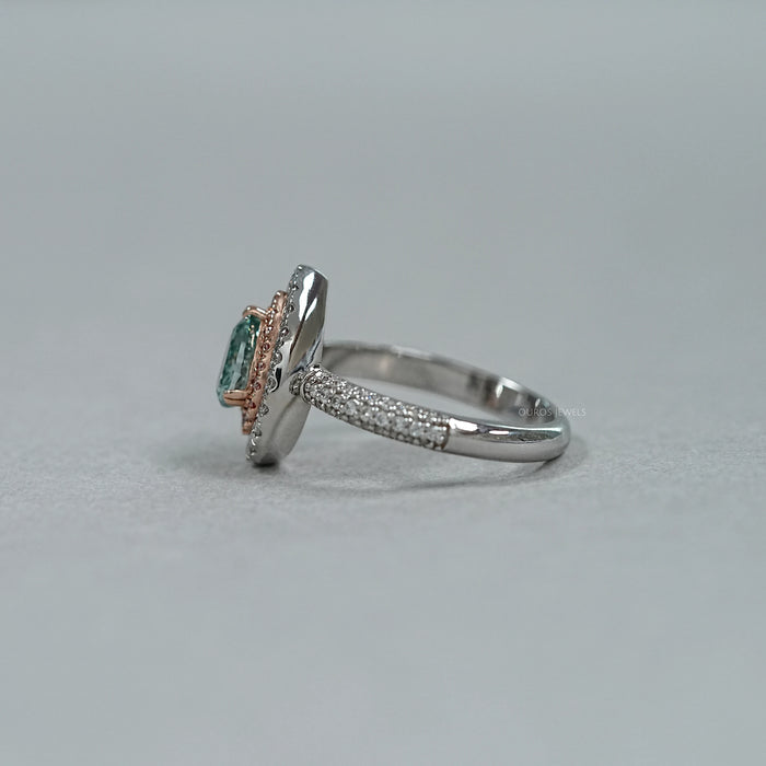 side view of green pear cut diamond double halo engagement ring on grey fabric