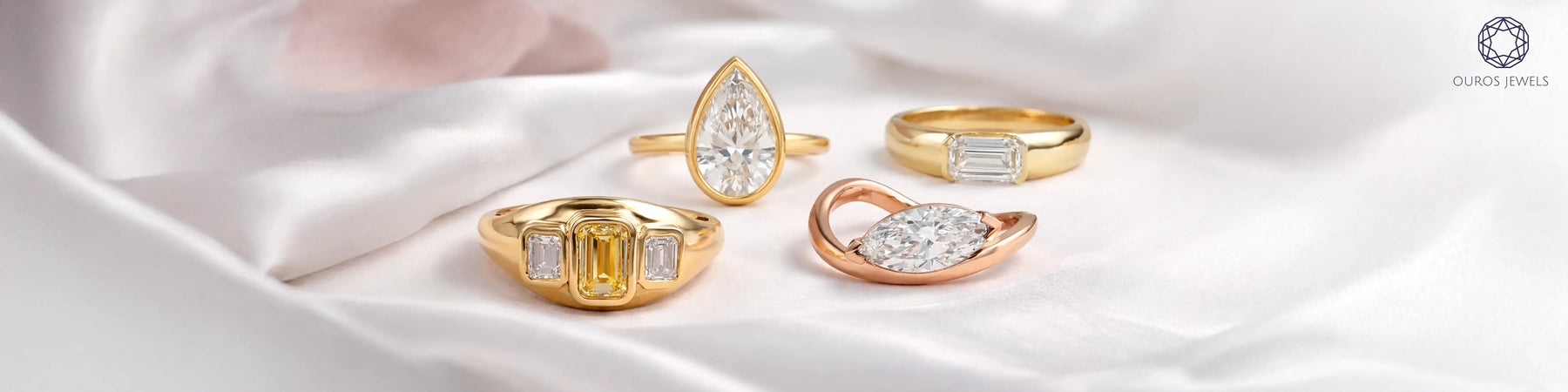 Four lab-grown diamond rings from Ouros Jewels in yellow and rose gold — featuring pear, emerald, baguette, and marquise cuts, displayed on white silk fabric 