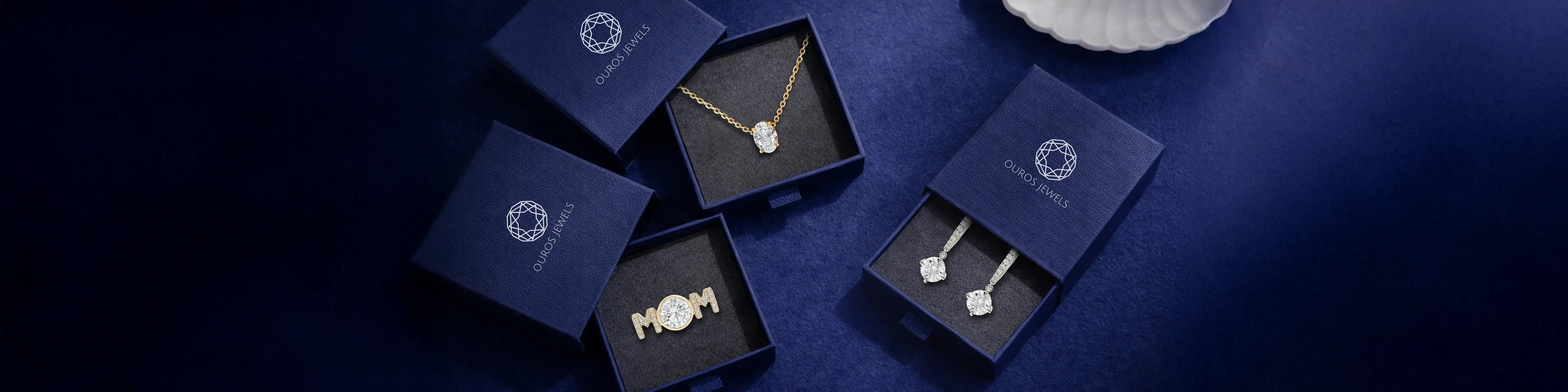 Ouros Jewels Mother's Day gift ideas featuring diamond pendant necklace, MOM ring, and drop earrings in navy blue gift boxes