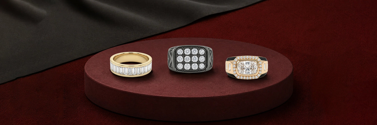 Men's lab-grown diamond bands — yellow gold channel-set baguette band, black gold cushion signet ring with round brilliant grid setting, and yellow gold cushion halo signet ring with baguette accents on burgundy display