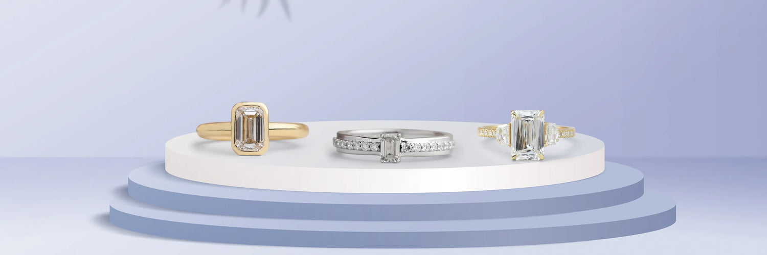 Three emerald cut lab-grown diamond engagement rings in yellow gold — three-stone with trapezoid baguette side stones, classic four-prong solitaire with thin band, and full bezel solitaire on layered stone surface