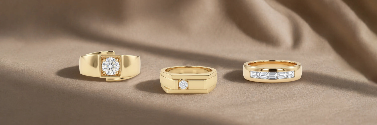 Three men's lab-grown diamond rings in yellow gold — round brilliant solitaire signet ring, princess cut bezel signet band, and channel-set baguette diamond wedding band on beige fabric