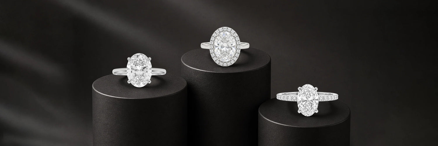 Three oval cut lab-grown diamond engagement rings in white gold — classic four-prong solitaire, oval diamond halo with pavé band, and east-west oval solitaire with full pavé band on black cylinder pedestals