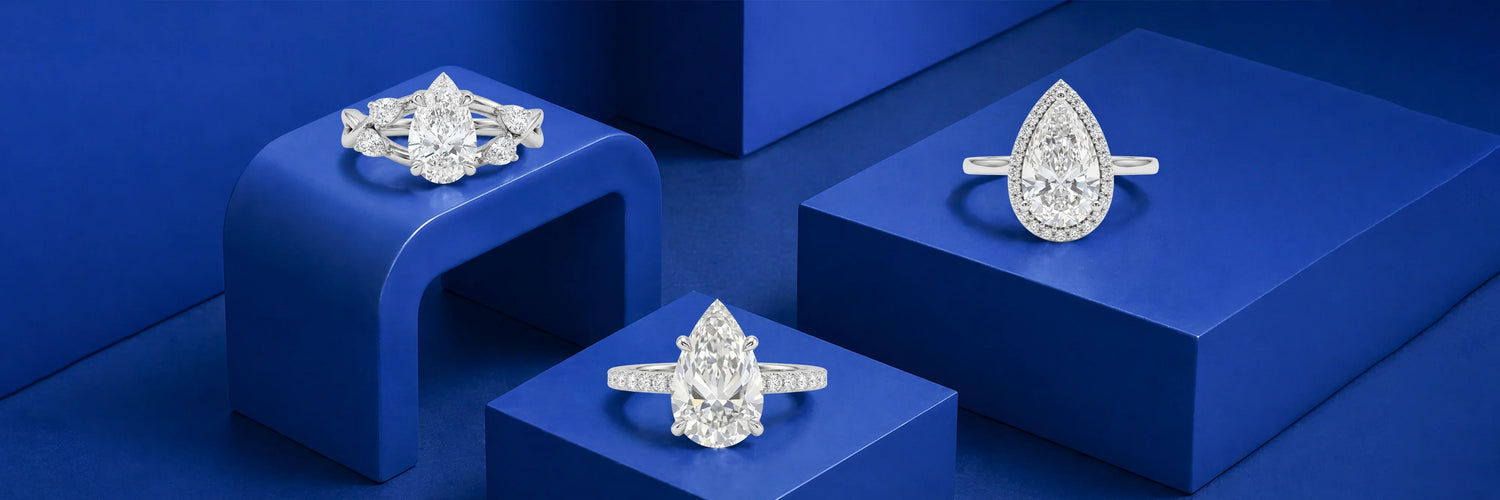 Three pear shaped lab-grown diamond engagement rings in white gold — vintage floral three-stone with marquise and baguette accents, large pear solitaire with pavé band, and pear cut diamond halo ring on cobalt blue display