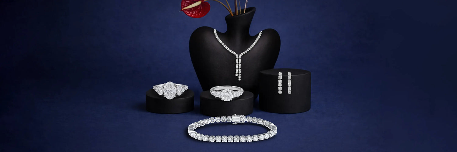 Ouros Jewels Ready To Ship Mother's Day Jewelry Collection offering lab grown diamond earrings, necklace, rings, and bracelet displayed on burgundy velvet stands with pink ribbon
