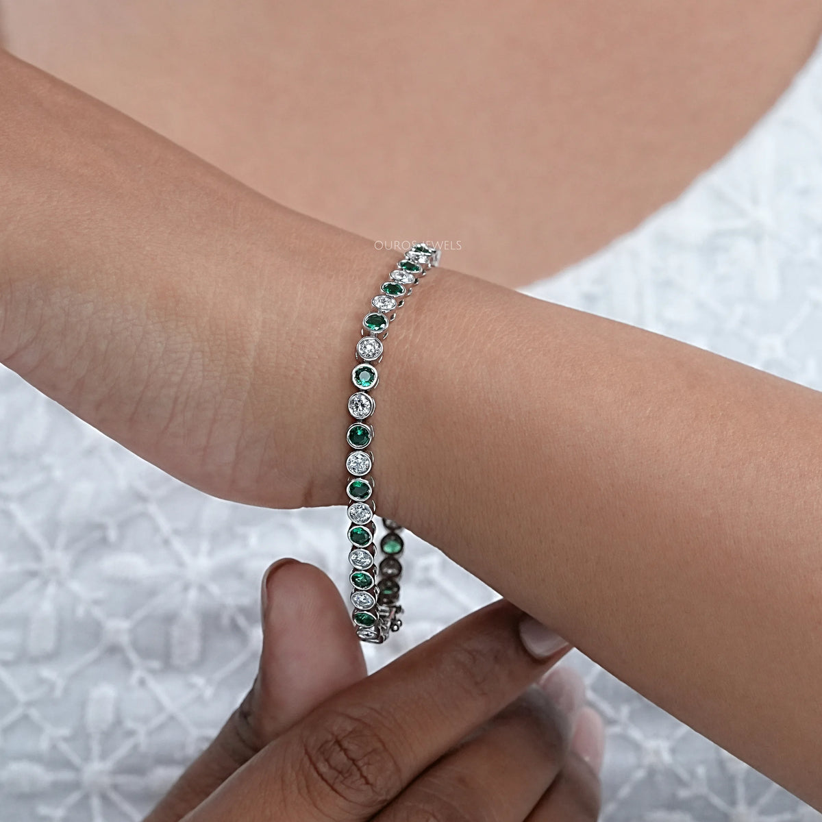Round green gemstone and bezel set diamond tennis bracelet worn on the wrist 