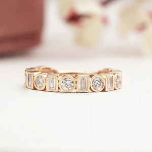 Baguette And Round Cut Diamond Bezel Set Wedding Band is displayed on a soft surface with a blurred flora background.