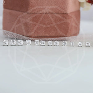 Asscher Cut Diamond Stud Earrings displayed in a line, arranged by size, next to a pink velvet jewelry box on a light surface.