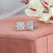 Marquise Cut Cluster Stud Earrings displayed on a soft pink cushion, featuring intricate floral designs with sparkling lab-grown diamonds, and delicate white flowers in the background.