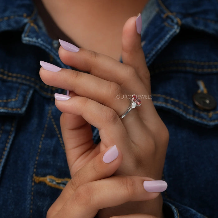 In finger side look of 3 stone radiant cut diamond engagement ring with pear shaped side stones