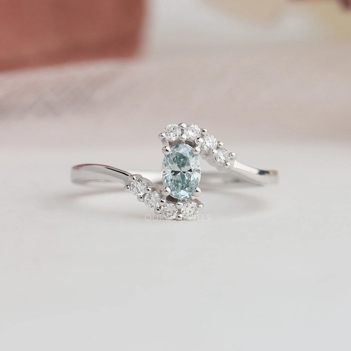 Close up look of green oval engagement ring set in curved band & bypass set.